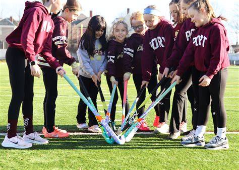 A youth field hockey team practicing drills on a green field.
