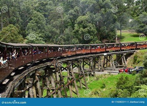 A Puffing Billy steam train crossing a wooden bridge over a river.