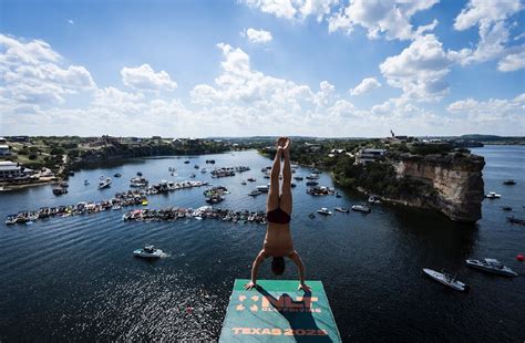 A large crowd is watching cliff divers compete in a scenic location.