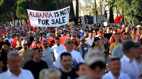 Protesters in Tirana, Albania, gathered and demanding electoral reforms, with signs and flags visible.